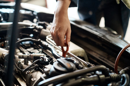 Take care of your car and your car will take care of you. a mechanic pulling out the dipstick to check a cars oil level.の写真素材
