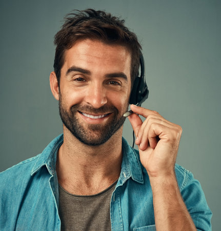Happy man, headphones and portrait of a call center consultant against a grey studio background. Face of friendly male consulting agent smiling with headset in contact us, customer service or adviceの写真素材