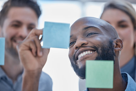 Black man, writing and smile for schedule planning on glass board for team brainstorming or tasks at office. Happy African male smiling in project plan, ideas or sticky note for teamwork strategyの写真素材