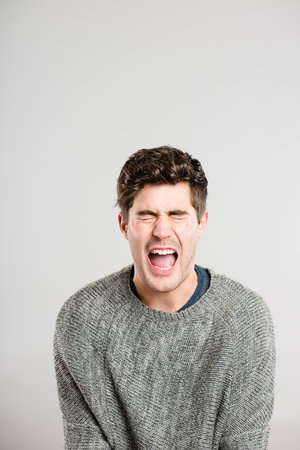 I just want to scream. a handsome young man sitting alone in the studio and screaming.の写真素材