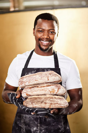 Its famous because its good. a male baker holding up freshly baked bread in his bakery.