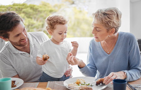 Family, food and eating with baby while feeding healthy diet or nutrition in the family lunch in home. Grandmother, child and dad with hungry boy kid and eat lunch or meal for health and wellnessの写真素材