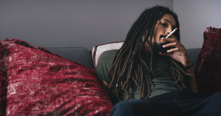 Laying back with a blunt. a young man smoking a marijuana joint at home.の写真素材