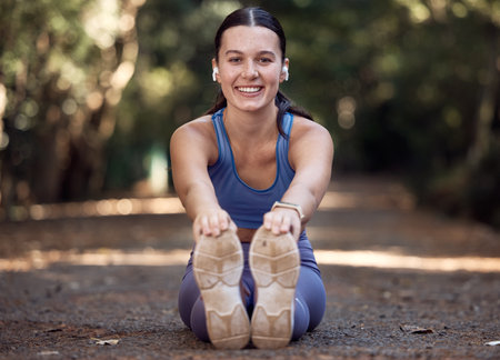 Earphones, portrait and woman stretching legs in nature while streaming music, radio or podcast. Sports, wellness or female outdoors at park for warm up getting ready for running, training or workoutの写真素材