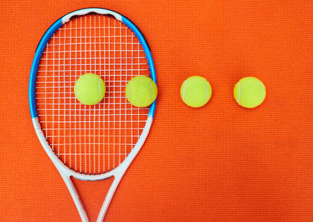 All lined up in a row. High angle shot of a single tennis racket and a few tennis balls placed on an orange background inside of a studio.の写真素材