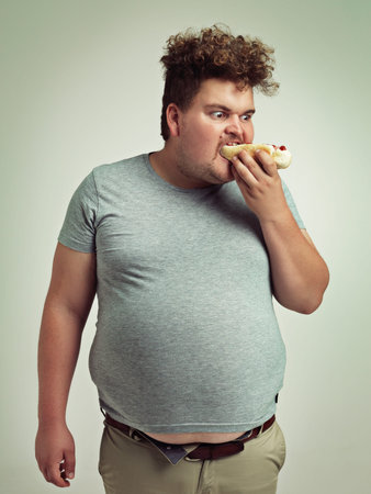 I cant get enough of these hotdogs. Studio shot of an overweight man eating a hotdog.の写真素材