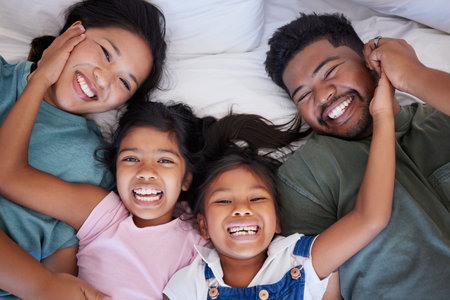 Happy, smile and portrait of family from above in bed bonding together in a bedroom at home. Happiness, love and interracial parents lying with girl children in holiday house room while on vacation.の写真素材