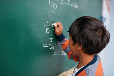 Easy as cake. a focussed young elementary school kid writing answers to math questions on a green chalkboard in the classroom.の写真素材