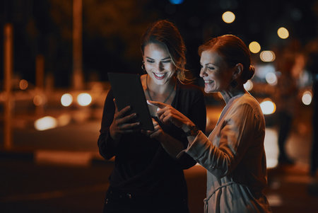 The city inspires them even more. two businesswomen using a digital tablet together outside an office at night.の写真素材
