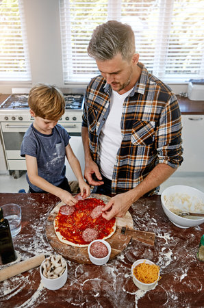 Then you add your meat...a father and his son making pizza at home.の写真素材