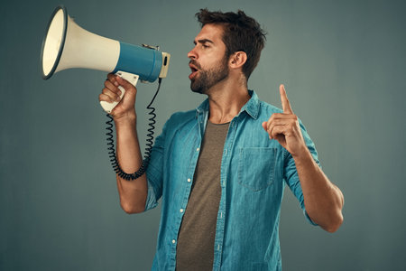 Ive got an announcement to make. Studio shot of a handsome young man talking into a megaphone against a grey background.の写真素材