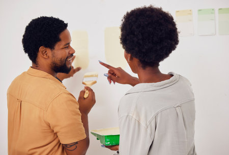 Painting, wall or happy black couple in DIY, home renovation or house remodel together with a paintbrush. Back view, smile or African man speaking to a woman working with team work in partnershipの写真素材