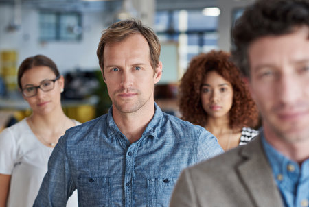 Whatever the task, he face it with confidence. Portrait of a serious man with colleagues in front of him and behind him.の写真素材
