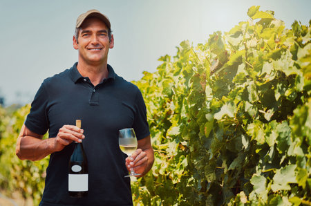 Portrait of one smiling farmer holding a bottle and glass of white wine on his farm. Happy caucasian...