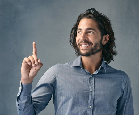 The ad is up there not down here. Studio shot of a handsome young man pointing against a grey background.の写真素材