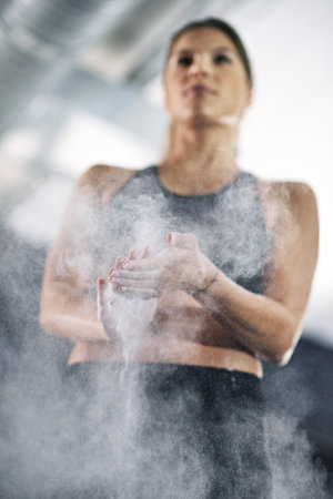 Ready to grab some heavy weights. a young woman coating her hands with sports chalk.の写真素材