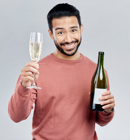 Portrait, champagne and toast with a man in studio on a gray background holding a bottle for celebration. Glass, alcohol and cheers with a handsome young man celebrating the new year traditionの写真素材