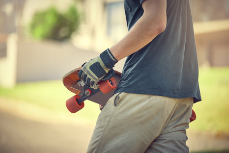 Fun, skateboard and man skateboarding in a neighborhood for fitness, exercise and training. Sport, cardio and hands of a teenager with a board in the street to travel, commute and playing in the roadの写真素材