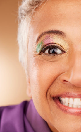 Eye, makeup and woman being creative, colorful and smile for fun, happy and content with brown studio background. Cosmetics, elderly female or senior lady with glitter for happiness or natural beautyの写真素材