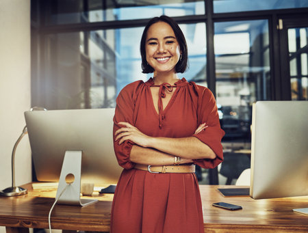 Portrait, smile and late with a business woman in her office, arms crossed while working in the evening at night. Vision, happy and dark with an asian female employee standing at work for dedicationの写真素材