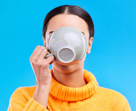 Coffee drinking, woman and studio with morning latte, mug and hot beverage. Isolated, blue background and female model or young person with casual fashion and ceramic cup for tea drink or cappuccinoの写真素材
