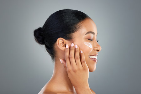 My skin feels pampered. a beautiful young woman applying moisturiser to her face.の写真素材