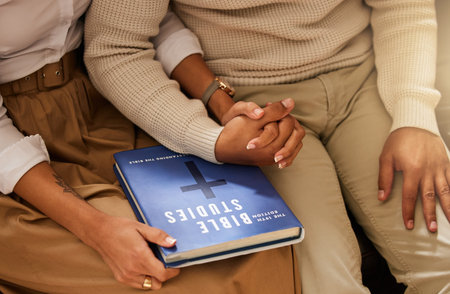 Love, bible and couple holding hands, studying and support with religious practice, teaching and growth for marriage. Holy text, man and woman bonding, scripture and prayer with connection or healingの写真素材