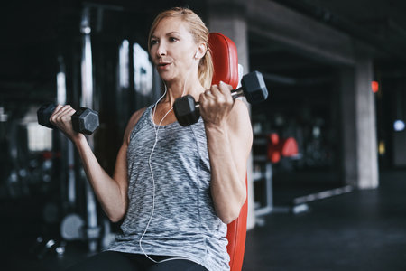 Getting stronger one rep at a time. an attractive young woman listening to music while working out with dumbbells in the gym.の写真素材