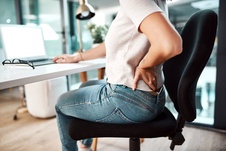 Back pain, stress and business woman at desk with burnout, muscle ache and tension in sitting posture. Health, medical emergency and female worker with spine problem, accident and injury in officeの写真素材