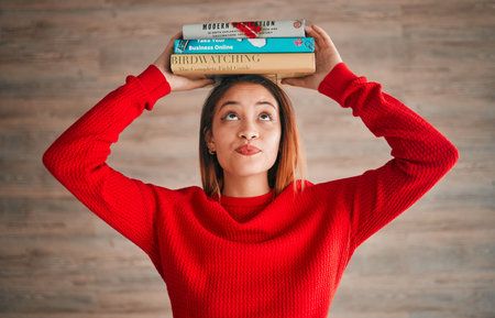 Reading, student and woman with books on her head while studying in college for a test or exam. Thinking, thoughtful and young female with stories, novels or fiction standing by a wall in the libraryの写真素材
