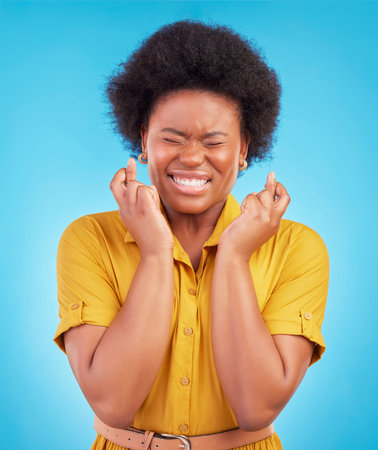 Black woman, fingers crossed and hope in studio, blue background and hopeful face. Female model,...