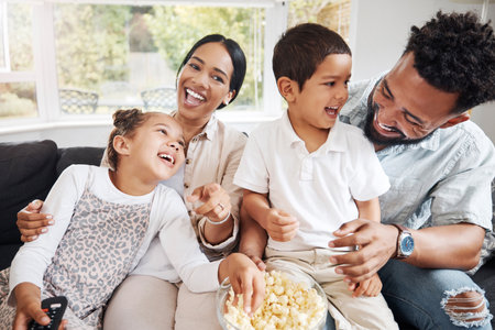 Family watching tv or a movie, having fun and eating popcorn together at home. Love and laughter with affectionate parents and happy children smiling, enjoying the weekend and feeling carefreeの写真素材