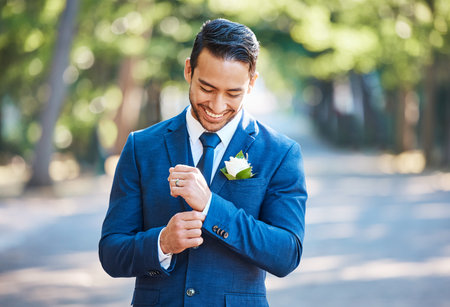 Handsome groom wearing a blue suit with a white shirt and tie. Bridegroom adjusting his sleeves while standing outdoors on a sunny dayの写真素材