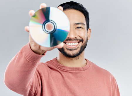 Man, holding and compact disc in studio portrait for smile, happiness and technology by white background. Asian model, student and cd in hand for movie, audio and sound with happy, excited and techの写真素材