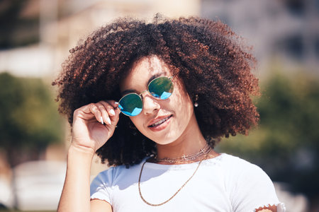 Woman, fashion and sunglasses on face outdoor in city for summer holiday and travel with a smile. Portrait of African person with natural hair or afro and trendy glasses at a park for freedomの写真素材
