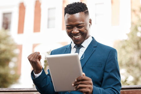 Happy businessman, tablet and celebration in city for winning, promotion or good news outdoors. Black man with smile on technology for trading, profit or lottery win in success on outdoor park benchの写真素材