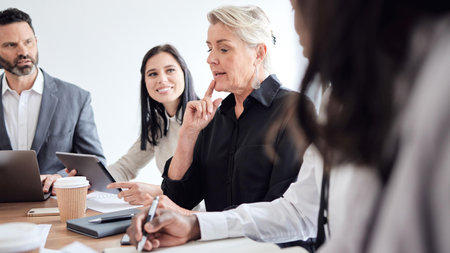 Business people, meeting and mature woman talking to a team in a corporate office for brainstorming. Diversity men, manager and women at a table for planning, discussion and thinking of strategyの写真素材