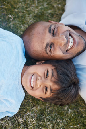 Family, portrait and lying on grass in backyard with father and kid together with love. Face, top view and dad with child on holiday with with parent support and care on a lawn with happy smileの写真素材