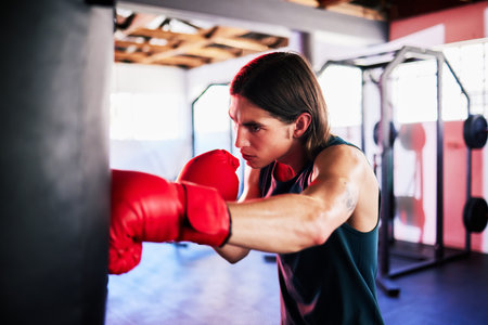 Punching bag, man and boxing in gym for exercise, workout or training for fight. Boxer, sports and serious fitness athlete punch for challenge, competition or exercising body for martial arts power.の写真素材