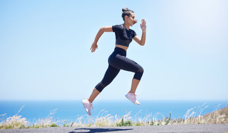 Runner woman, street and jump in nature with speed, fitness and energy for training, wellness and healthy by sea. Girl, running and fast on road for self care, exercise and workout by ocean in summerの写真素材