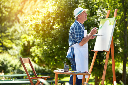 Hell be painting until the sun goes down. a senior man painting in the park.の写真素材