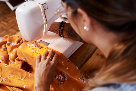 Let me tell you how to turn your sewing skills into cash...a young woman stitching fabric using a sewing machine at home.の写真素材