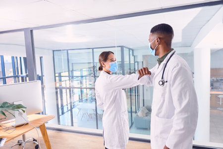 Greeting one another in the safest way possible. two unrecognizable doctors wearing masks and elbow bumping while standing in the hospital.の写真素材