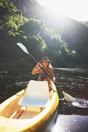 Id rather be out here canoeing. a young woman out kayaking on a lake.
