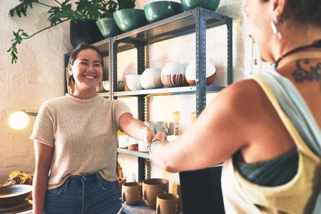 Welcome to the crafting community. two young women shaking hands in a pottery studio.の写真素材