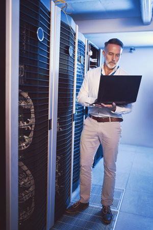I cant allow any security threats to get here. a mature man using a laptop while working in a server...