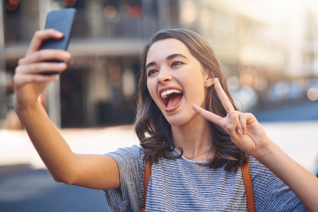 Peace out. an attractive young woman taking selfies while spending her day out in the city.の写真素材