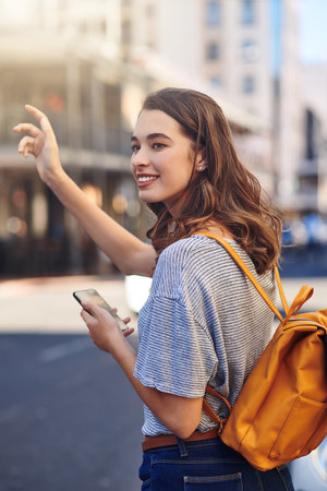 Need a ride Use the app. an attractive young woman sending a text message while hailing a taxi out in the city.の写真素材