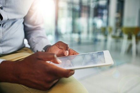 Hes been getting far ahead in the business world. Closeup shot of an unrecognizable businessman using a digital tablet in an office.の写真素材
