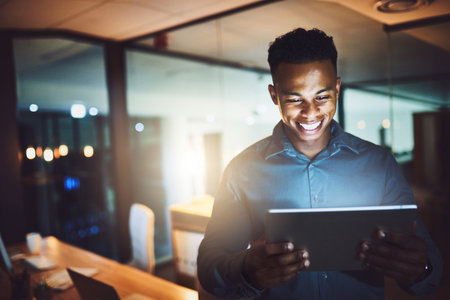 Its the only way to do business. a handsome young businessman using his tablet while working late at night in a modern office.の写真素材